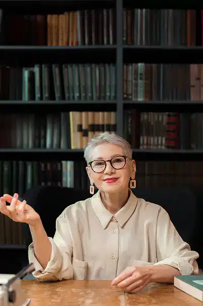 A woman seated at a desk, surrounded by bookshelves filled with various books.